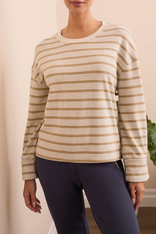 Wearing the Tribal CREW NECK TOP W/CUFF, a person stands indoors in front of a light-colored sofa, styled with navy blue pants and white sneakers.
