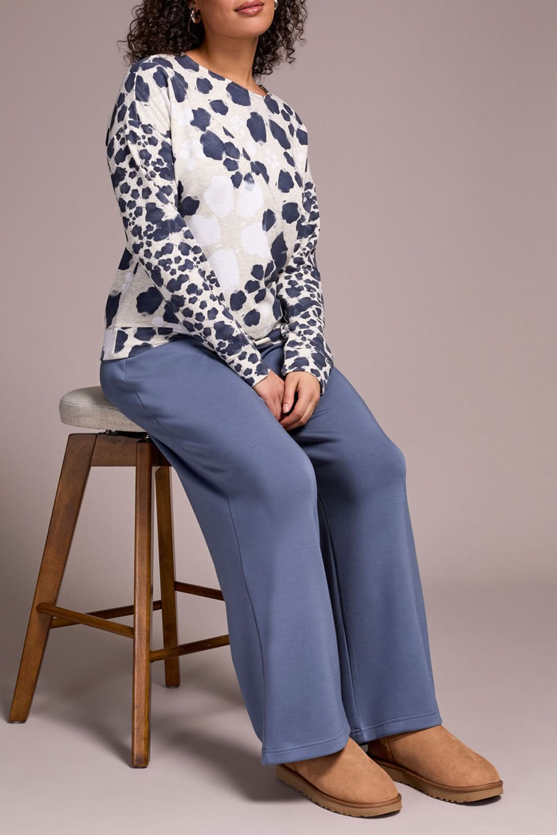 Someone stands against a neutral background wearing the Tribal CREW NECK TOP with a white and navy animal print, wide-leg blue pants, and tan slippers—an ideal look for casual wear.