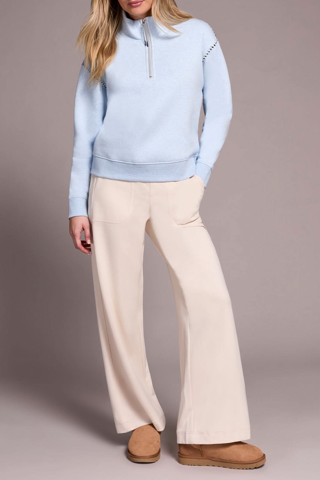 A person models the Tribal ZIP FUNNEL NECK TOP in light blue, paired with beige wide-leg pants and tan suede slippers, standing against a plain background.