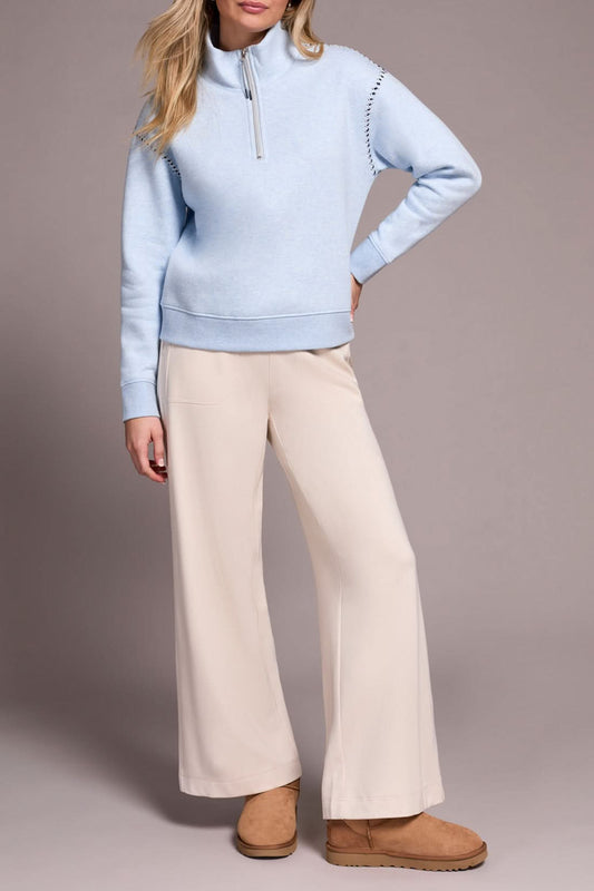 A person models the Tribal ZIP FUNNEL NECK TOP in light blue, paired with beige wide-leg pants and tan suede slippers, standing against a plain background.