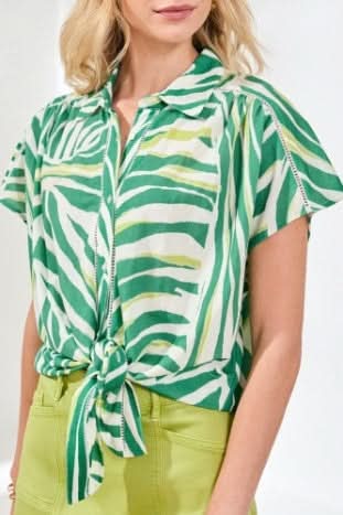 A woman with curly hair relaxes by the pool on a pink patterned cushion, wearing the Tribal Tie-Front Short-Sleeve Shirt in grass green, surrounded by greenery.