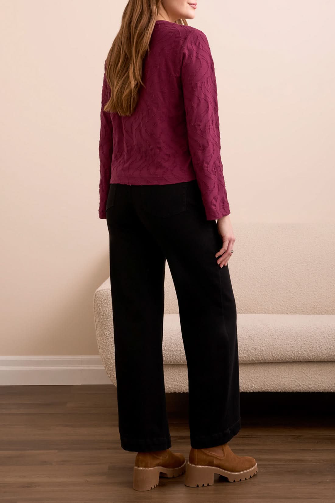 A woman stands indoors wearing the Tribal V NECK TOP in wine, paired with black wide-leg pants and brown platform shoes, with a beige couch in the background.