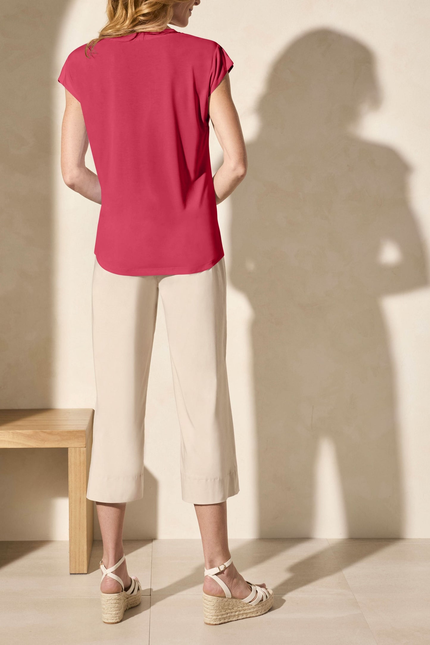 A person in a Tribal CAP SLEEVE V NECK TOP, beige wide-leg pants, and platform sandals stands against a light background, exuding timeless elegance.