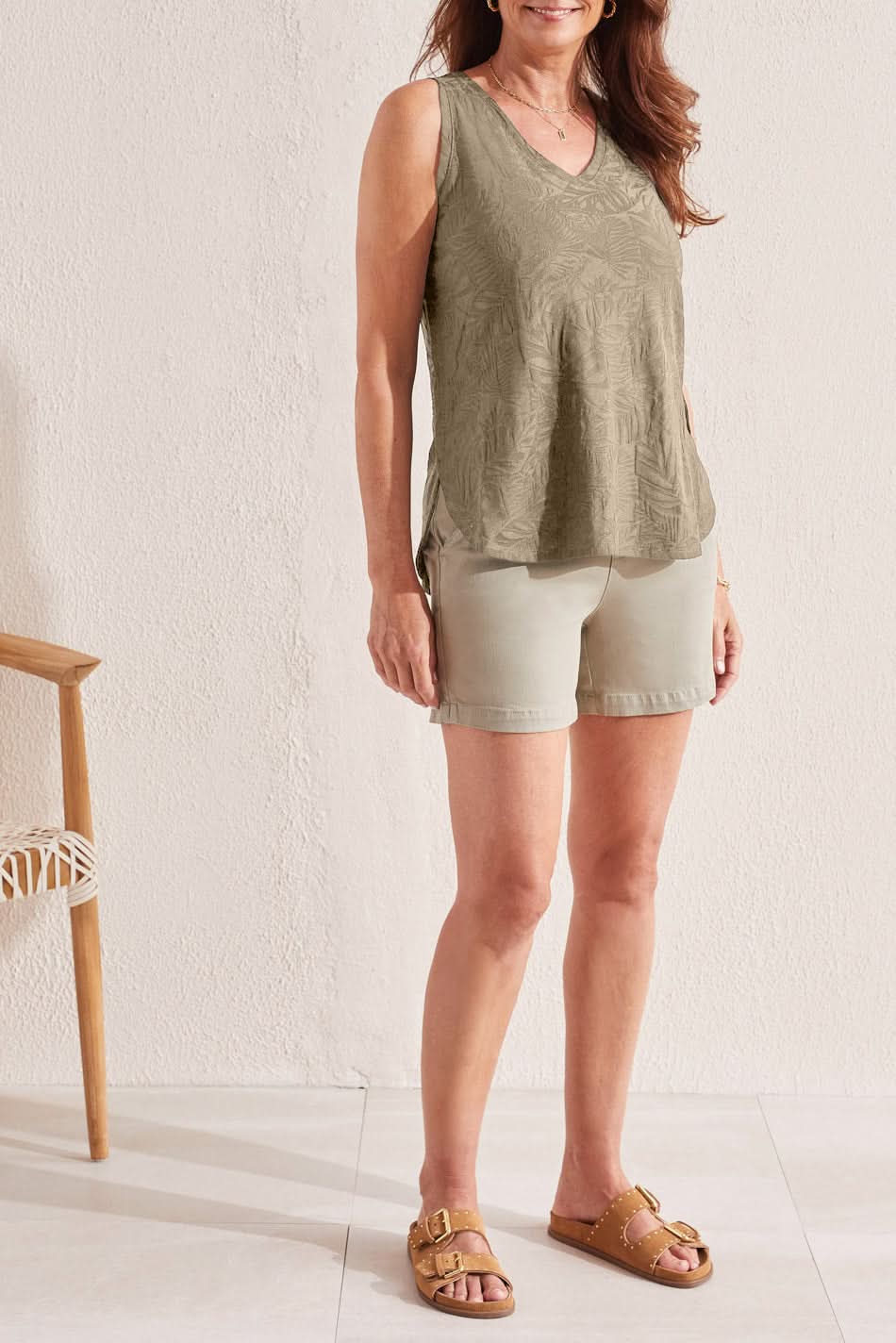 A woman wearing a Tribal TEXTURED V-NECK TANK WITH SIDE SLITS in an olive-green pattern and light-colored pants stands against a white background.