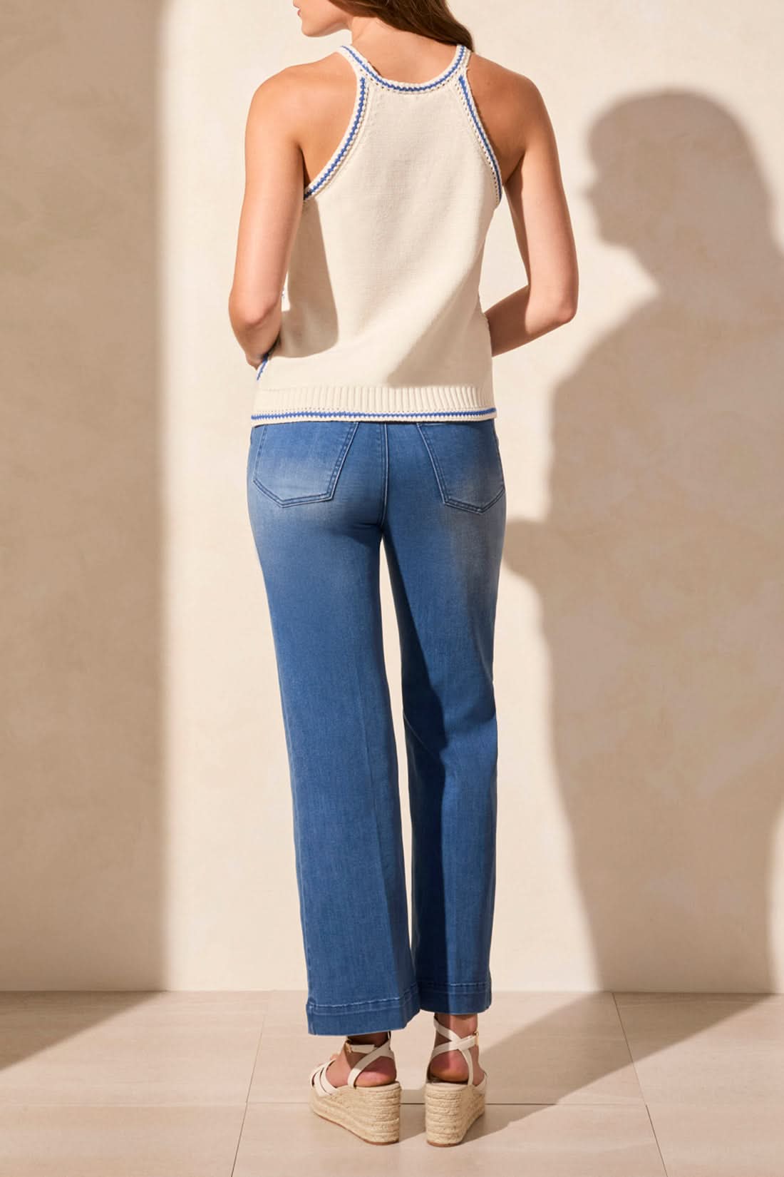 A woman in sunglasses, jeans, sandals, and the Tribal CROCHET COTTON RETRO SWEATER TANK walks beside a blue convertible on a sunny day.