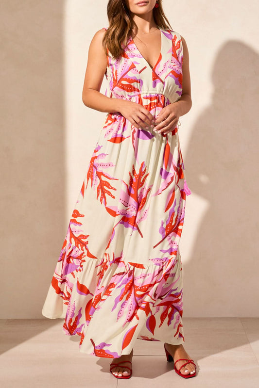 A woman models the Tribal MAXI DRESS WITH WAIST DRAWCORD, a sleeveless v-neck style with a pink and red abstract print, paired with red sandals—an effortless summer wardrobe addition—against a plain light backdrop.