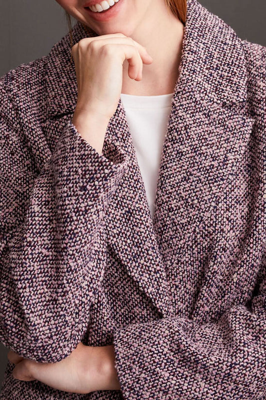 A person wearing a cozy Unlined Button Up Duster Coat by Tribal over a white shirt, pinkish pants, and beige shoes stands with hands in pockets in front of a dark paneled wall.