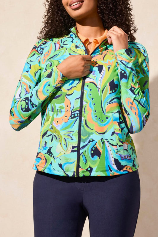 A person in a Tribal Mock Neck Zip Up Golf Cardigan, white skirt, socks, and sneakers stands against a light beige wall.