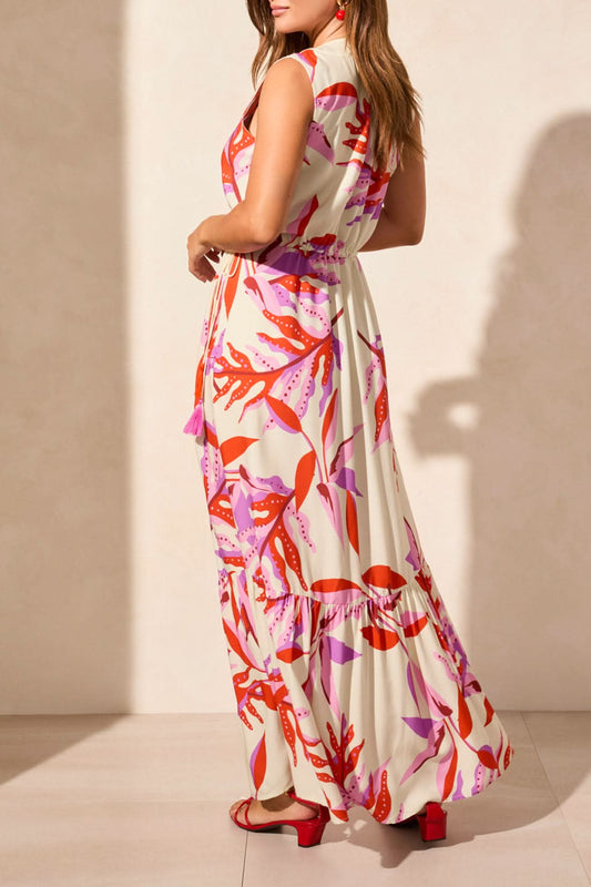 A woman models the Tribal MAXI DRESS WITH WAIST DRAWCORD, a sleeveless v-neck style with a pink and red abstract print, paired with red sandals—an effortless summer wardrobe addition—against a plain light backdrop.