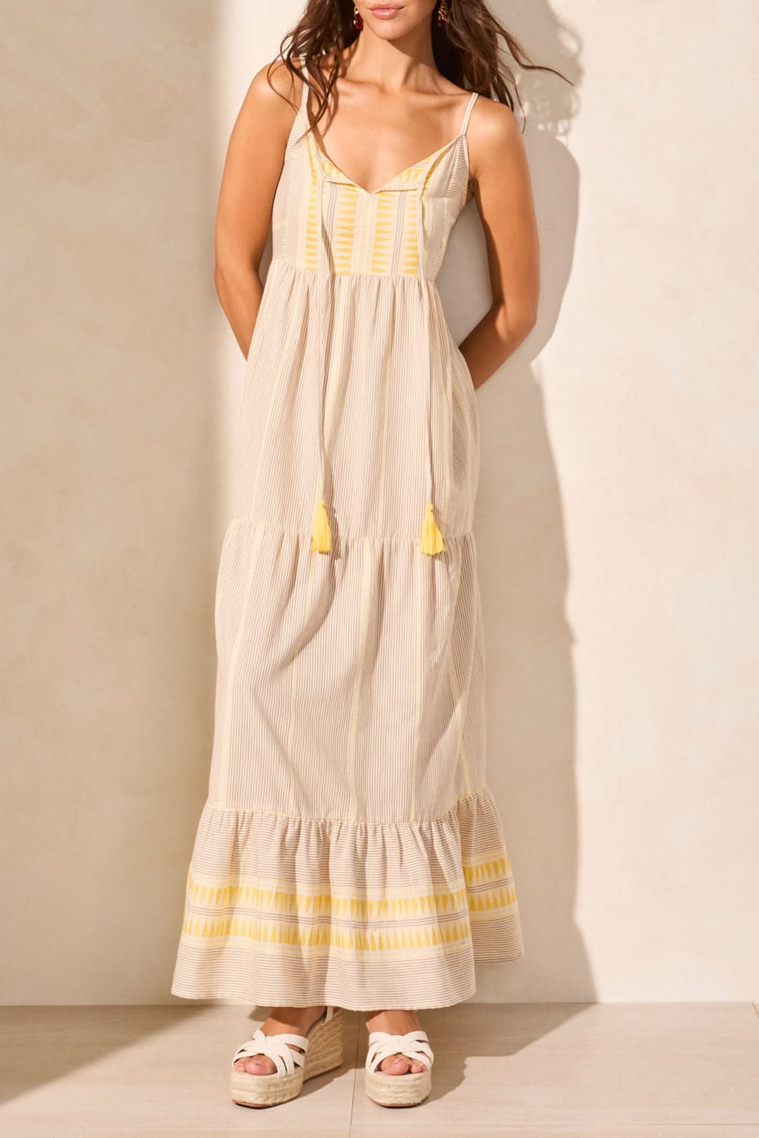 A woman in the Tribal SUMMER VACATION DRESS stands indoors by a wooden table with white vases, casting a shadow—an ideal pick to brighten your summer wardrobe or make vacation days special.