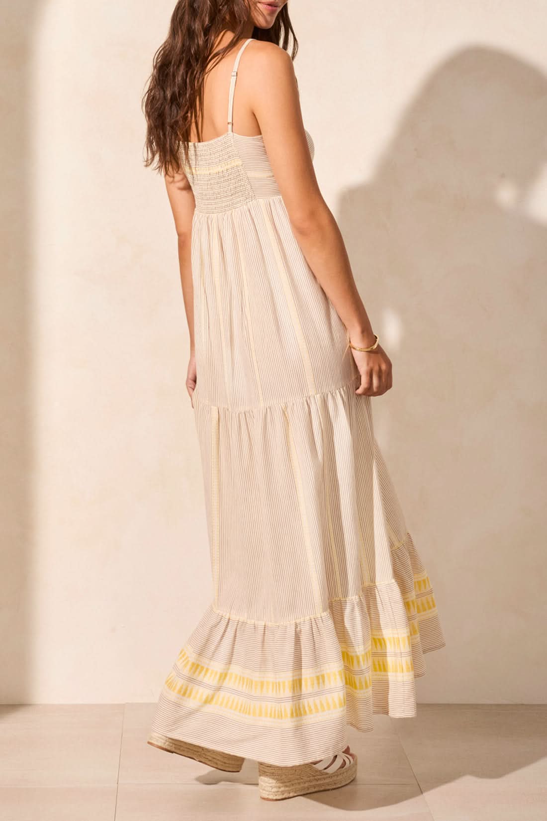 A woman in the Tribal SUMMER VACATION DRESS stands indoors by a wooden table with white vases, casting a shadow—an ideal pick to brighten your summer wardrobe or make vacation days special.