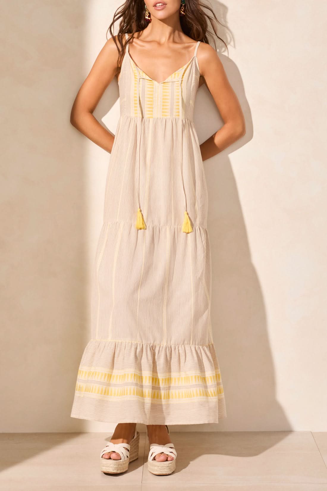 A woman in the Tribal SUMMER VACATION DRESS stands indoors by a wooden table with white vases, casting a shadow—an ideal pick to brighten your summer wardrobe or make vacation days special.