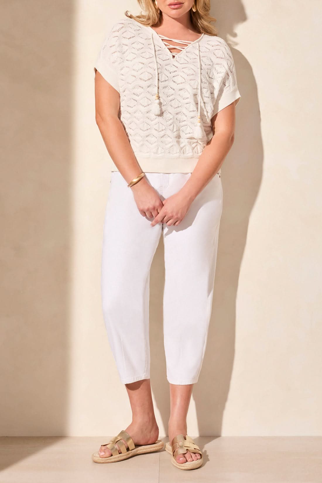 A woman models the Tribal SLEEVELESS LACE UP SWEATER WITH BEADS, featuring a geometric pattern, paired with white pants against a light background.