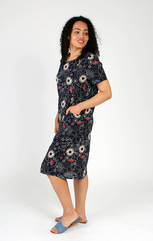 Woman in a versatile Fresh FX floral short sleeve dress posing with one hand on her hip against a white background, perfect for a summer wardrobe.
