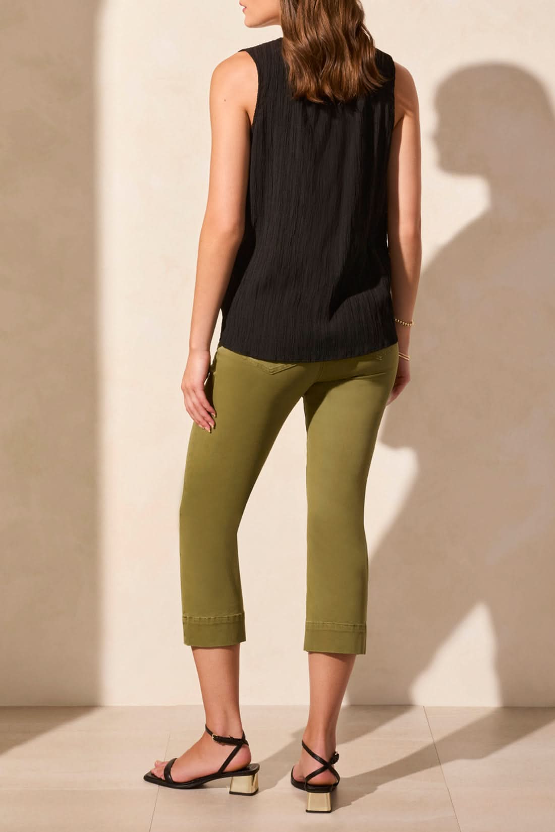 A woman wears the Tribal SLEEVLESS BLOUSE WITH BUTTON PLACKET, featuring a textured red finish, paired with relaxed striped pants as she stands against a light-colored wall.