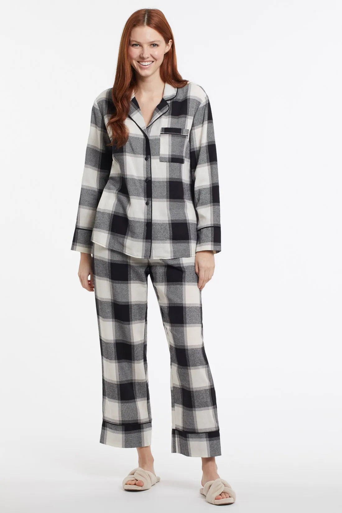A woman wearing a Tribal 2-Piece Plaid Flannel Pajama Set in front of a cozy fireplace.