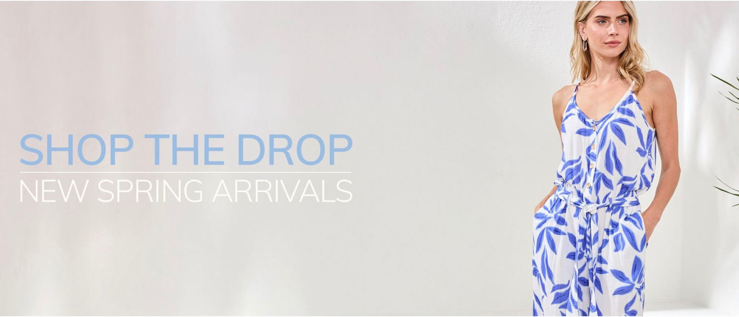A woman wearing a white and blue floral jumpsuit stands next to text that reads "Shop the Drop, New Spring Arrivals" against a light background.