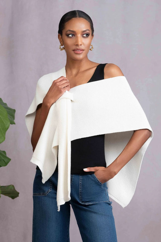 A woman stands against a light background, wearing a black tank top, blue jeans, and the Alison Sheri Off White Wrap—a versatile medium-weight shawl draped over her shoulders for effortless year-round layering.