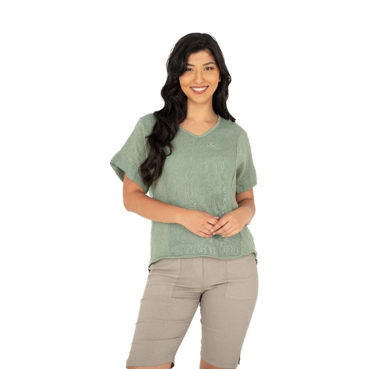 A person smiles while wearing the M Made In Italy V Neck Woven Top in green, paired with beige shorts against a white background.