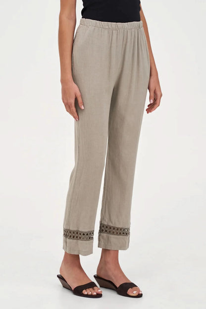 A person wearing M Made In Italy's Boho Trouser—beige linen straight-leg pants with an elastic waistband and cut-out hem details—paired with black open-toe sandals.