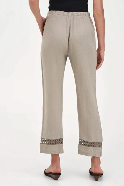 A person wearing M Made In Italy's Boho Trouser—beige linen straight-leg pants with an elastic waistband and cut-out hem details—paired with black open-toe sandals.
