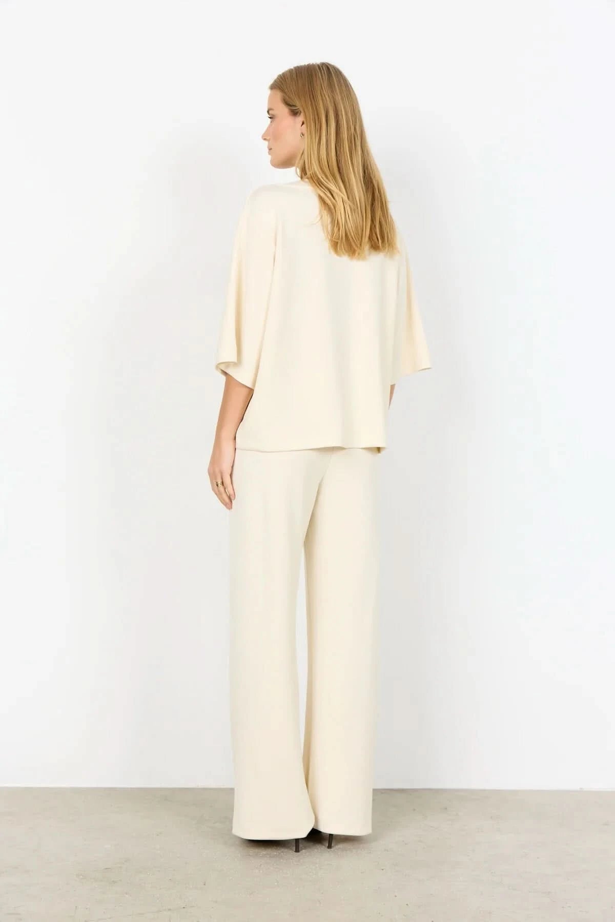 A woman with long blonde hair wears the Soya Concepts Banu Top, its elegant silhouette highlighted as she stands against a plain white background.