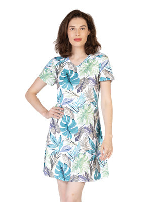 A woman stands with one hand on her hip wearing the Variations Leaf Print Short Dress, a knee-length, short-sleeve dress featuring green, blue, and purple tropical leaf patterns.