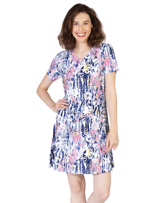 A woman with shoulder-length brown hair smiles at the camera wearing the Variations Printed Short Dress with short sleeves and a vibrant floral print.
