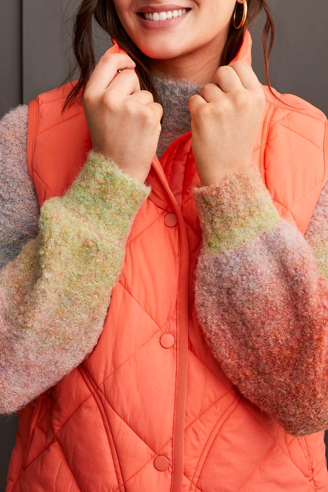 Person wearing a cozy black A Line Puffer Vest from Tribal over a red sweater with plaid pants, making a fashion statement while standing in front of a gray background.