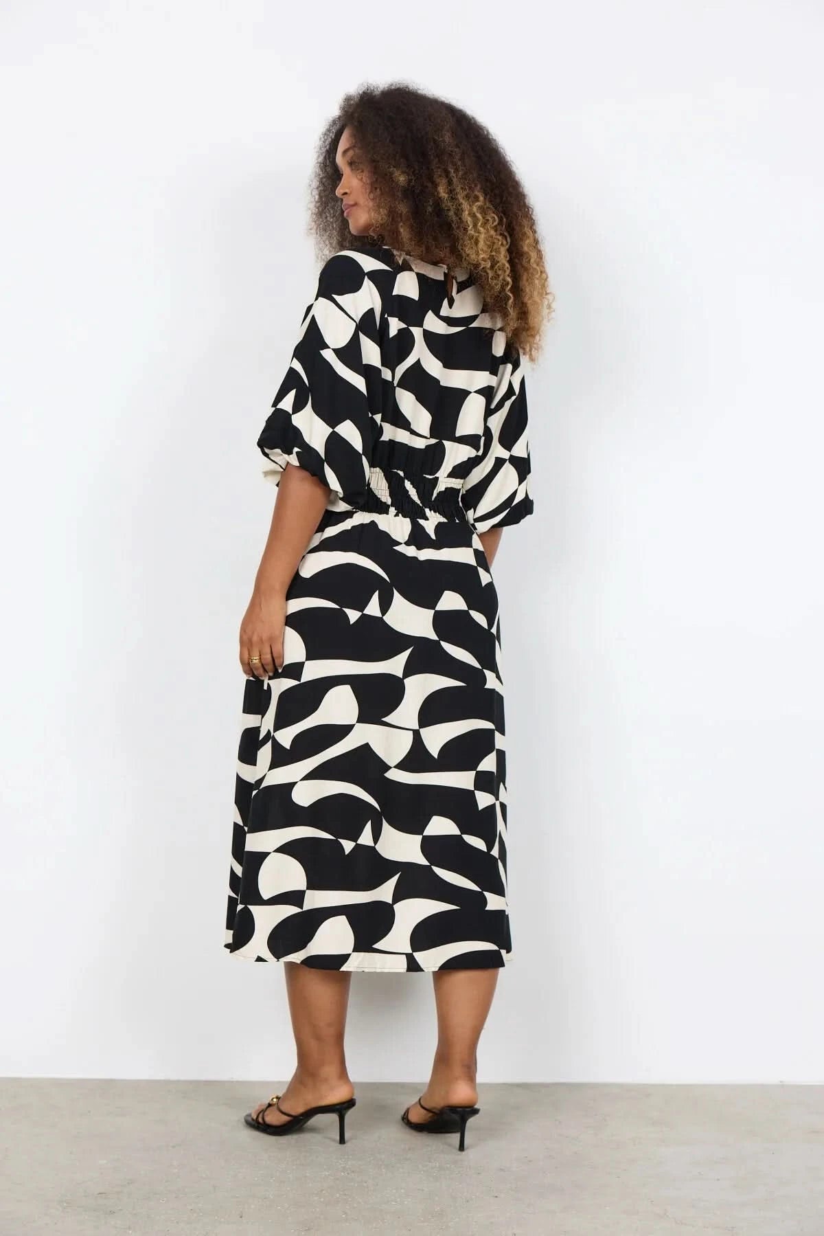 A woman wears the Chanise Dress by Soya Concepts, featuring a loose fit, black and white abstract print, and elbow-length sleeves, standing against a plain white background.