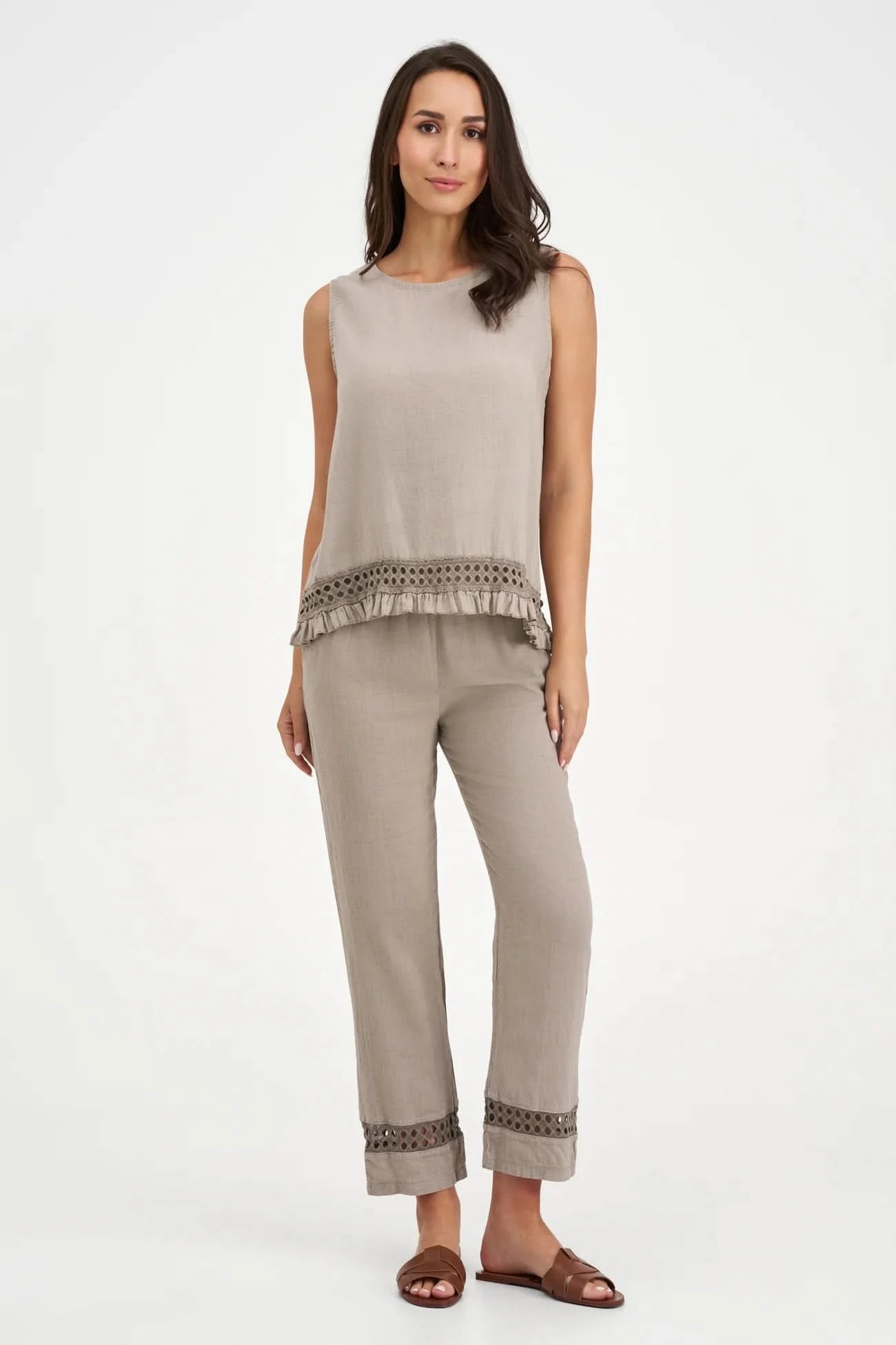 A person wearing M Made In Italy's Boho Trouser—beige linen straight-leg pants with an elastic waistband and cut-out hem details—paired with black open-toe sandals.