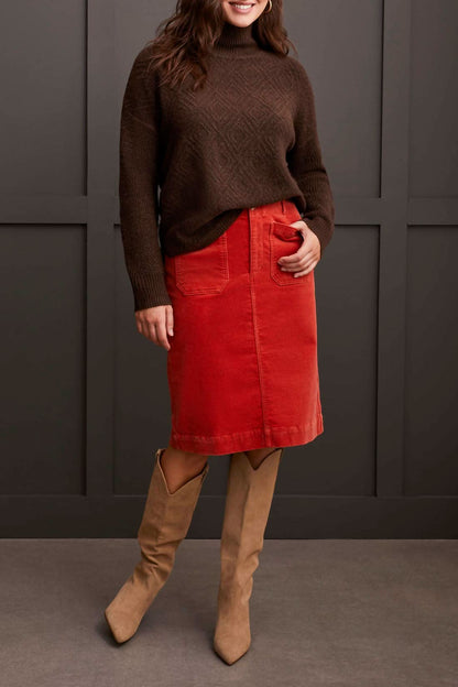 A person dressed in a cozy comfort ensemble featuring Tribal's coffee-colored Mock Neck Sweater, a red skirt, and tan knee-high boots stands against a dark paneled wall.