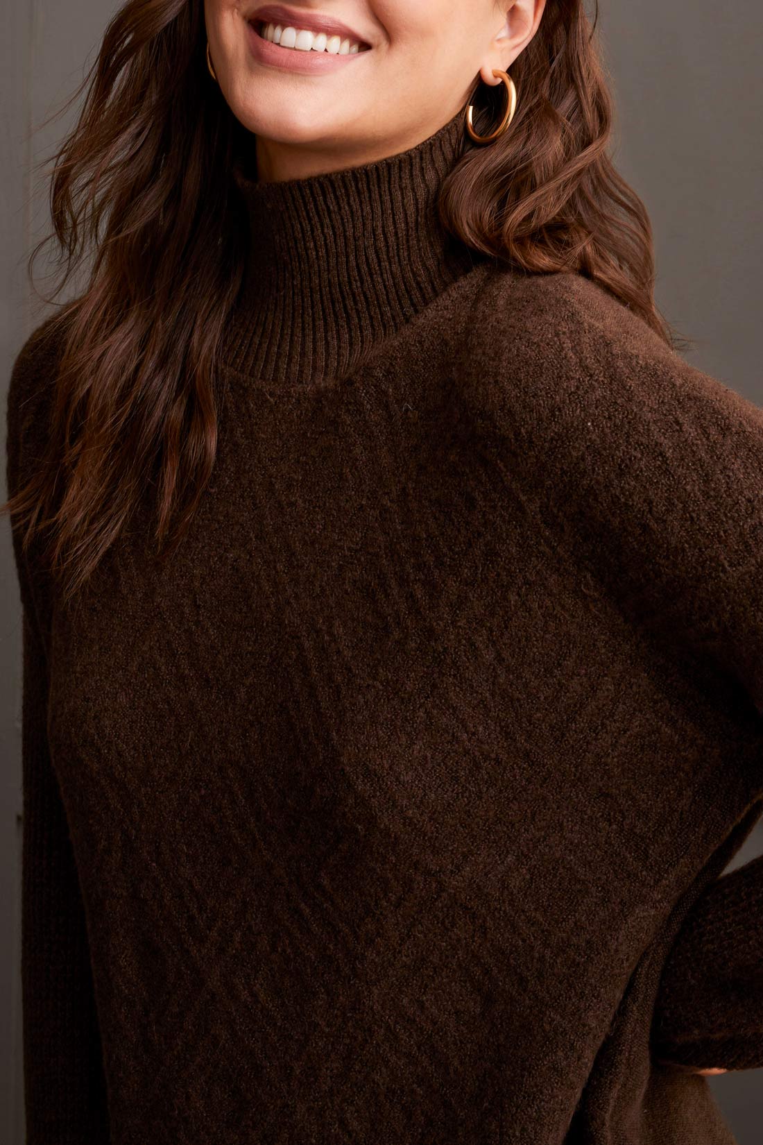 A person dressed in a cozy comfort ensemble featuring Tribal's coffee-colored Mock Neck Sweater, a red skirt, and tan knee-high boots stands against a dark paneled wall.