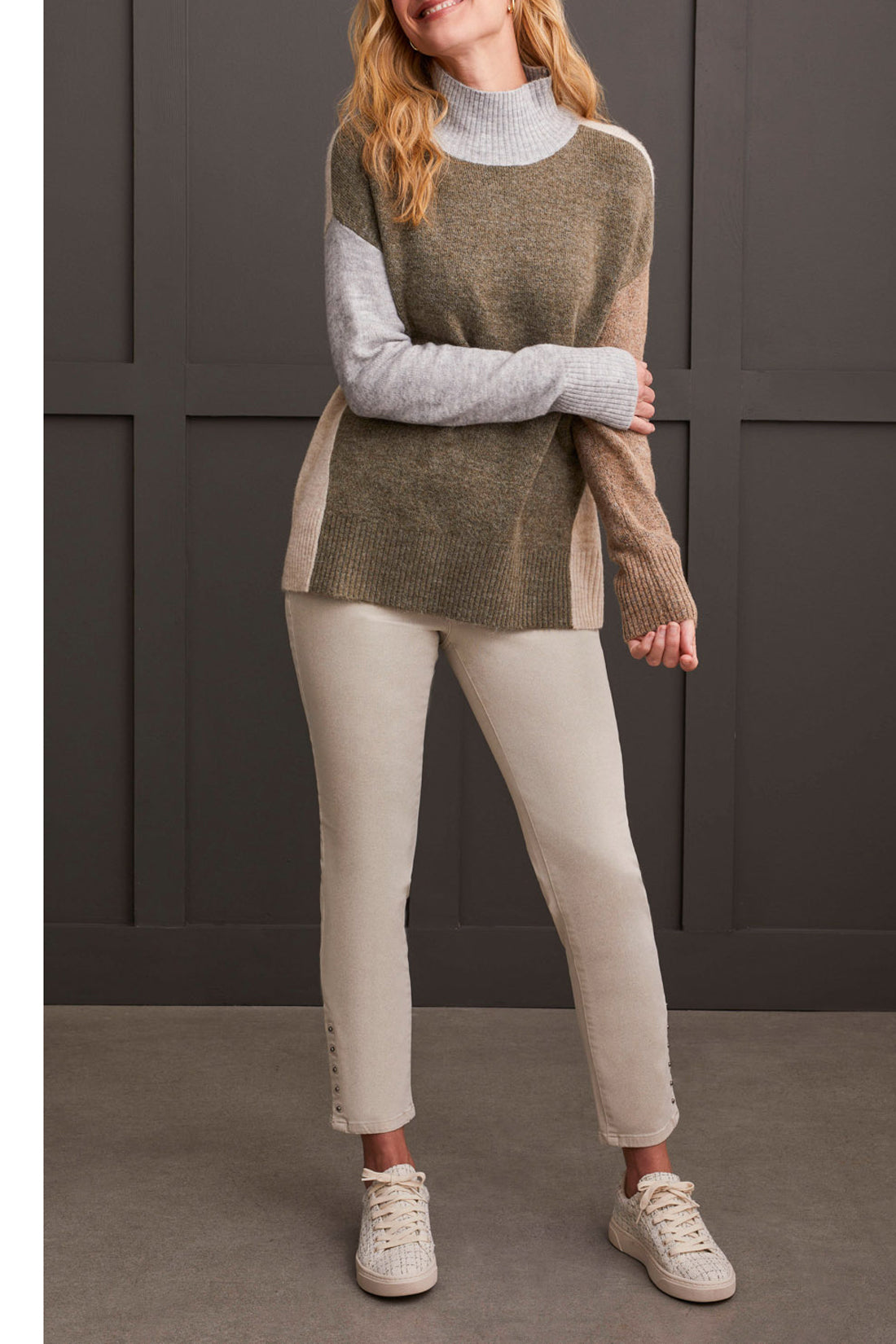 A person wearing the Mock Neck Colorblock Sweater by Tribal, featuring cozy gray, brown, and beige stripes, smiles while holding the collar near their face—truly a fall staple.