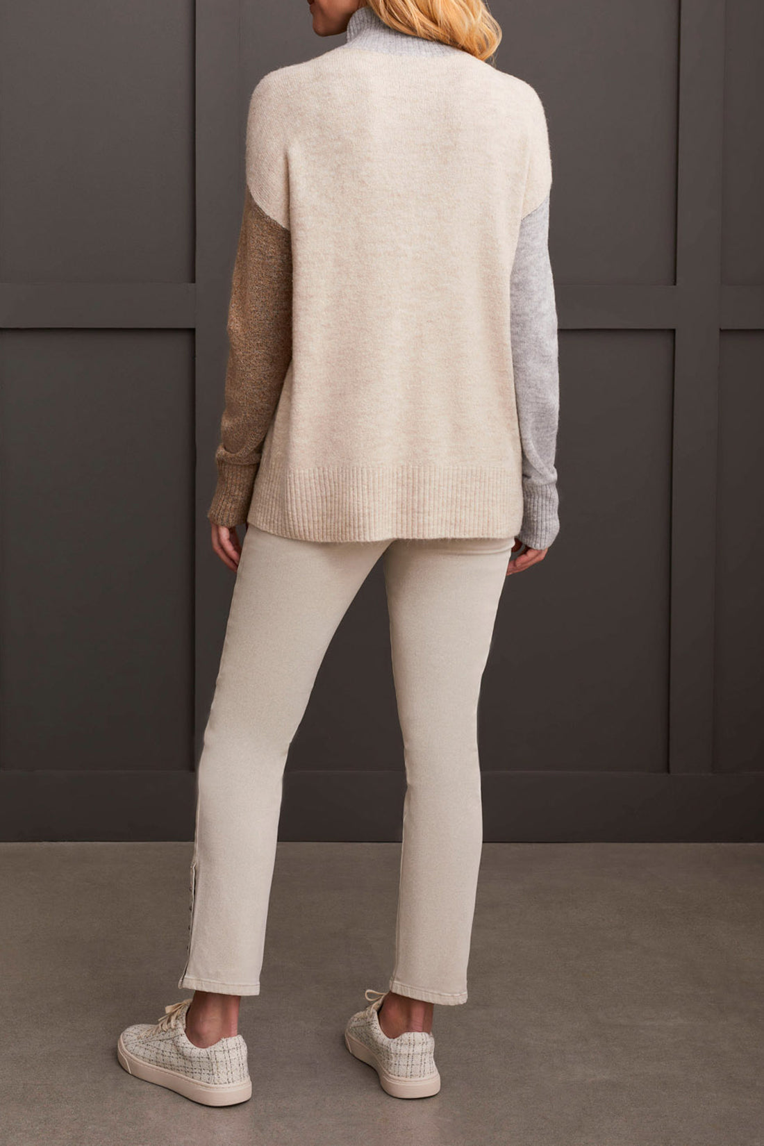 A person wearing the Mock Neck Colorblock Sweater by Tribal, featuring cozy gray, brown, and beige stripes, smiles while holding the collar near their face—truly a fall staple.