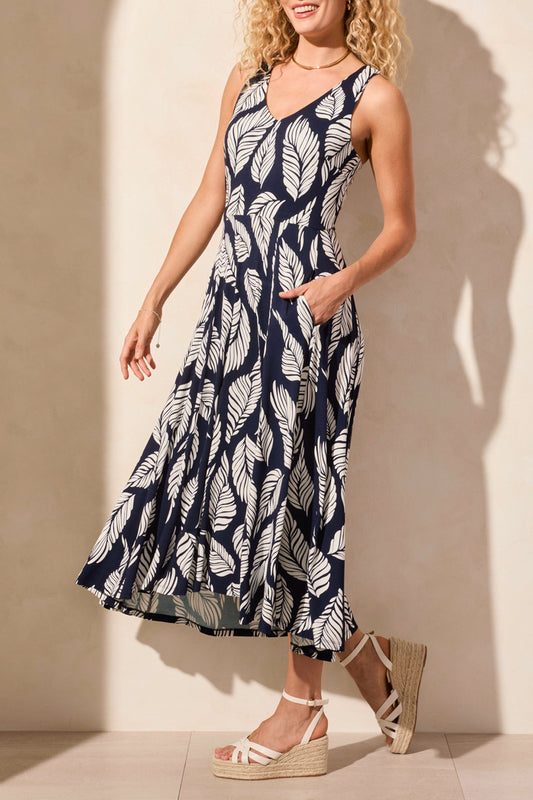 A woman stands against a light background, wearing Tribal's sleeveless high low dress featuring an abstract black and white print, paired with wedge sandals.