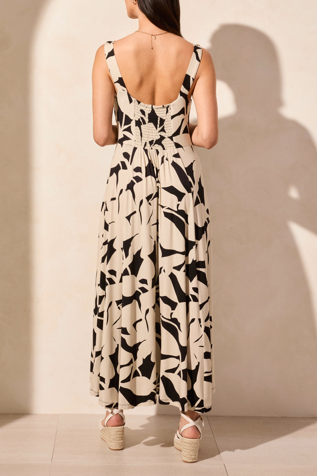 A woman stands against a light background, wearing Tribal's sleeveless high low dress featuring an abstract black and white print, paired with wedge sandals.
