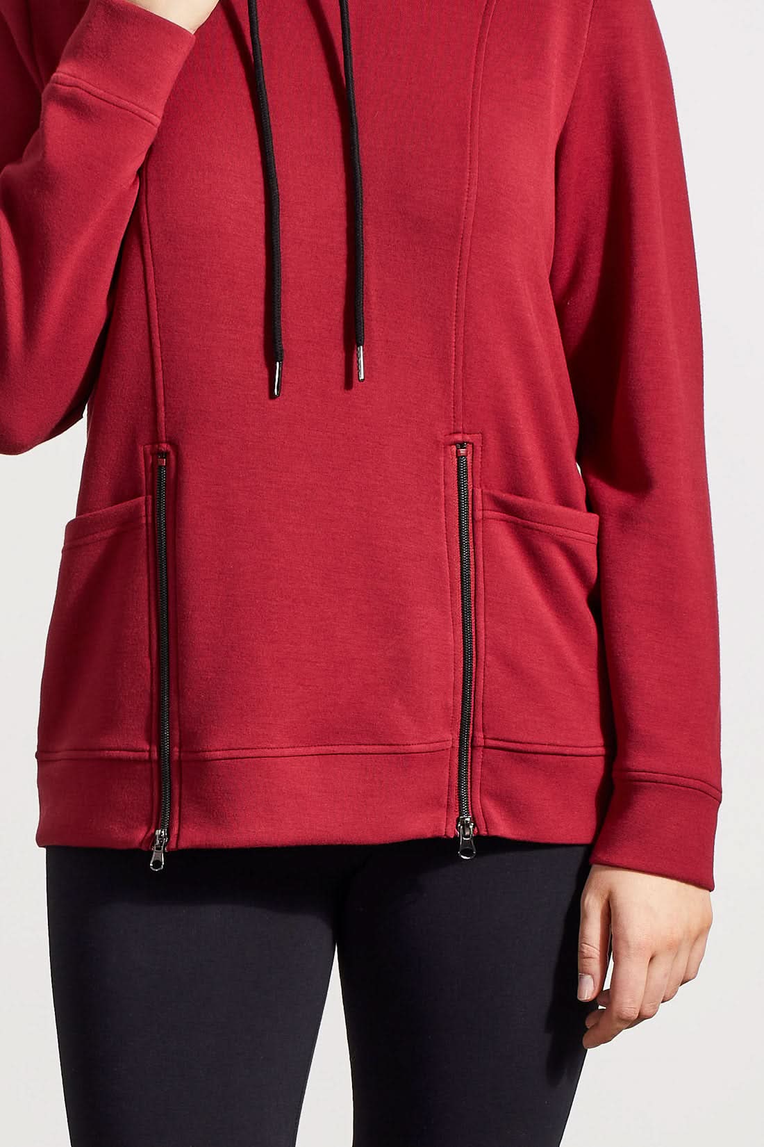 Individual dressed in a red Funnel Neck Top with Pockets by Tribal, featuring drawstrings and crafted from high-quality material, complemented by black pants.