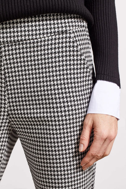 Close-up of a person showcasing the Tribal Houndstooth Pull on Pant, blending comfort and style with its classic houndstooth pattern. They're paired with a black sweater over a white cuffed shirt, revealing part of the torso and one hand.