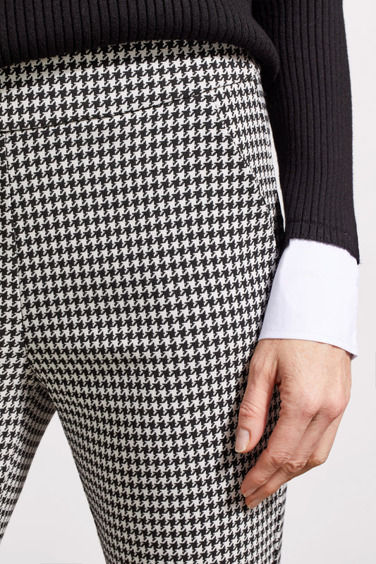 Close-up of a person showcasing the Tribal Houndstooth Pull on Pant, blending comfort and style with its classic houndstooth pattern. They're paired with a black sweater over a white cuffed shirt, revealing part of the torso and one hand.