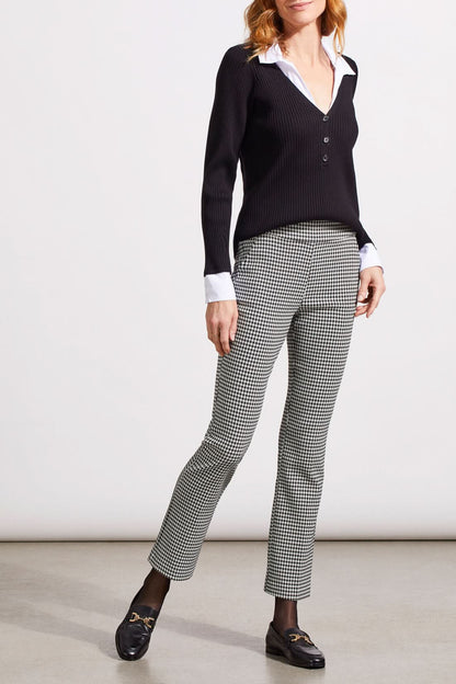 Close-up of a person showcasing the Tribal Houndstooth Pull on Pant, blending comfort and style with its classic houndstooth pattern. They're paired with a black sweater over a white cuffed shirt, revealing part of the torso and one hand.