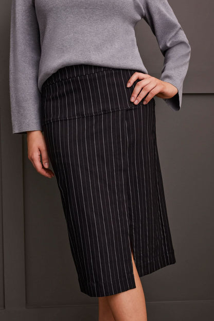 A person wearing a grey long-sleeve top and a black pinstripe pencil skirt with a slit, standing confidently with one hand on their hip, showcasing effortless style. This Striped Pull on Skirt by Tribal is a versatile addition to any wardrobe.