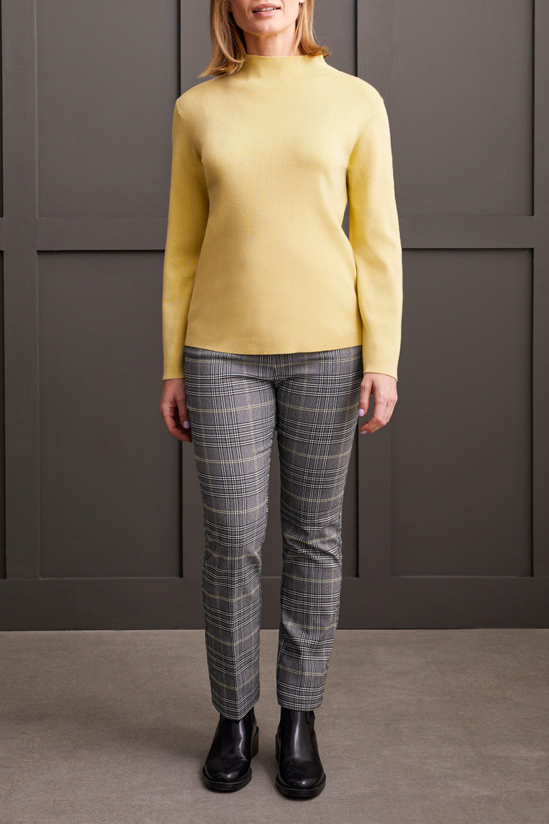 A woman with shoulder-length hair wearing a cozy and stylish yellow Funnel Neck Sweater from Tribal crosses her arms.
