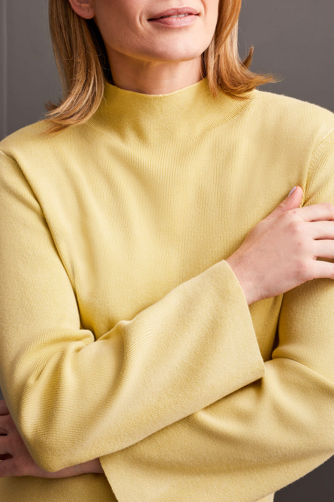 A woman with shoulder-length hair wearing a cozy and stylish yellow Funnel Neck Sweater from Tribal crosses her arms.