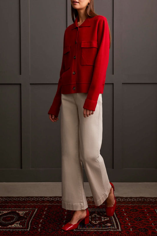 A person wearing the Tribal Sweater Cardigan with Collar and light-colored pants, standing against a dark paneled background, evokes the cozy allure of ultimate comfort.