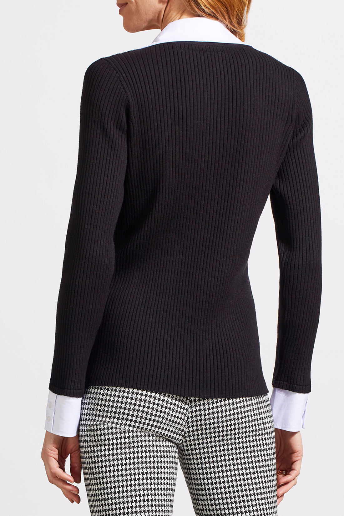 A person with shoulder-length hair is wearing a black ribbed cardigan with buttons over a white collared shirt, creating a fashionable look. The Tribal Henley Fooler Sweater adds an extra touch of sophistication, crafted from high-quality materials for enduring style.