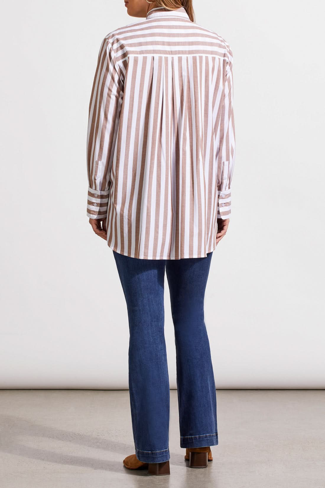 A person in a contemporary style, dressed in a striped Button Front Shirt with Pleats by Tribal, blue jeans, and brown boots, strides against a neutral background.