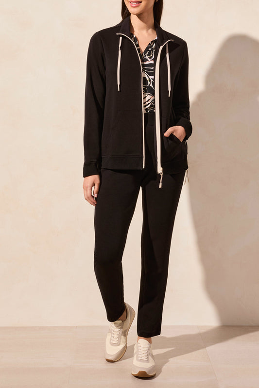A person in a Tribal MOCK NECK CARDIGAN, paired with patterned top and white sneakers, stands against a light-colored wall.