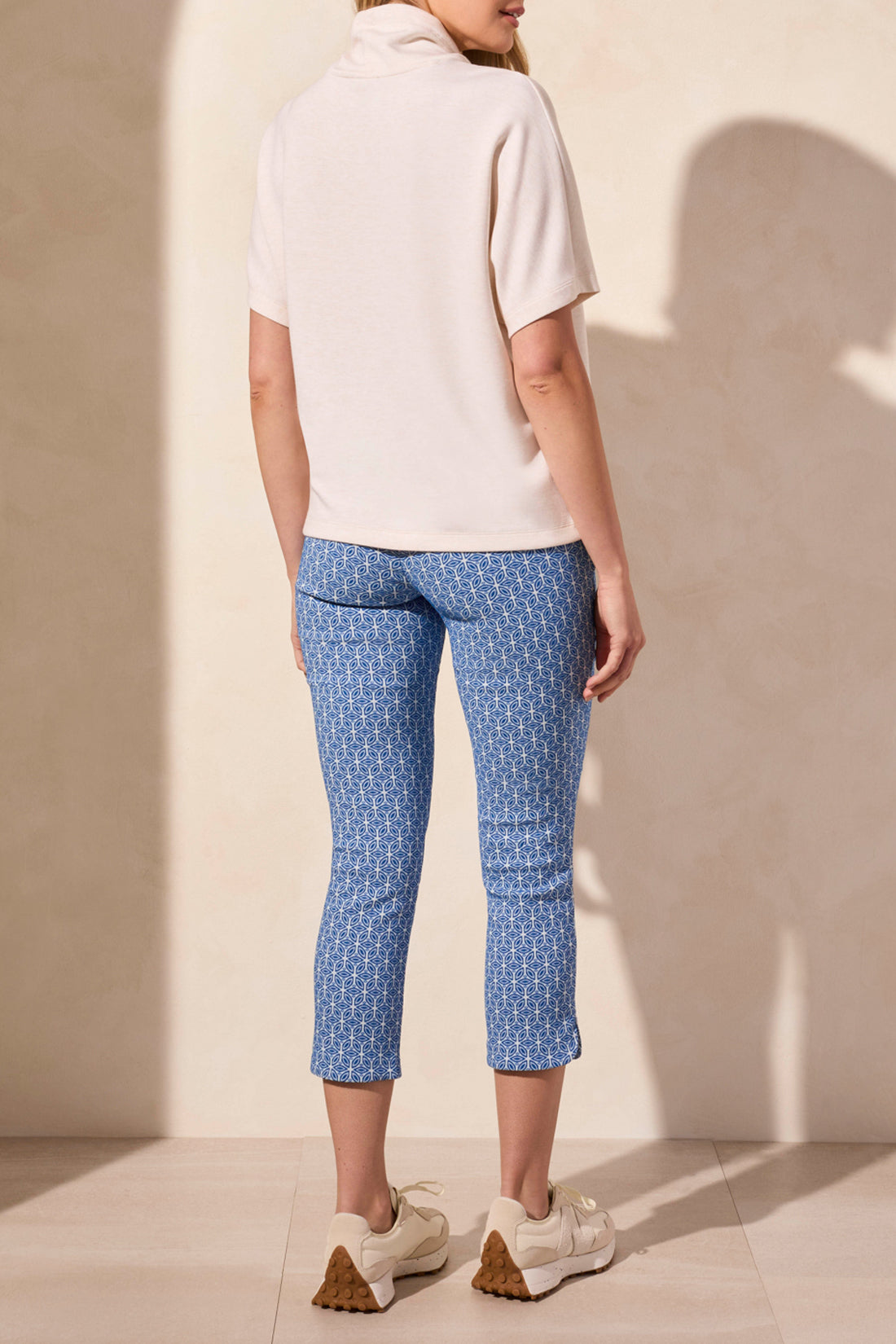 Wearing Tribal's SHORT SLEEVE FUNNEL NECK TOP in light beige, a person pairs it with blue patterned pants against a plain background. The versatile top features a flattering fit and drawstrings.