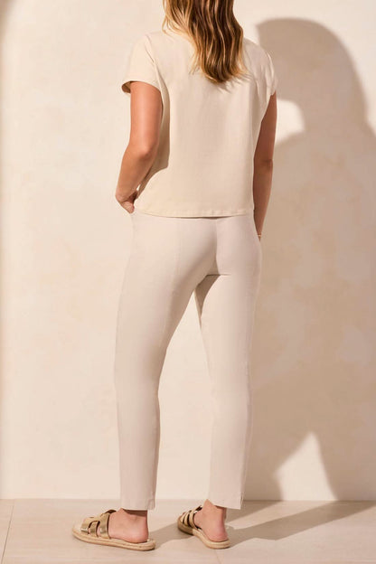 A woman wearing a Tribal CAP SLEEVE TOP, featuring a beige outfit with a pink floral design on the shirt, smiles while placing one hand in her pocket.